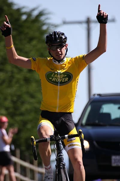 Jim Camut crossing the line with arms raised, in Land Rover team kit.