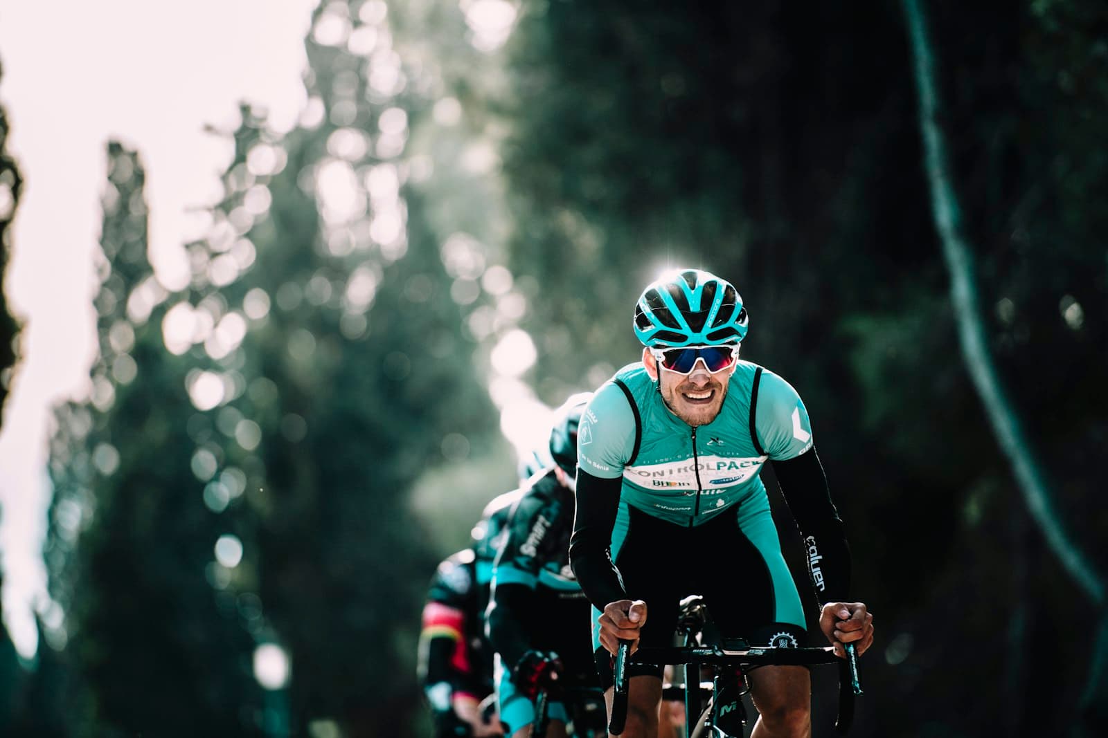 A road cyclist riding hard at threshold on a tree-lined road — the kind of self-coached effort an adaptive training plan is built to respond to.
